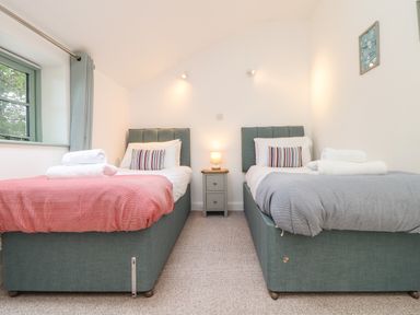 A bedroom with two single beds with striped pillows and folded towels a nightstand with a lamp and a window with curtains at Penpoll in Falmouth