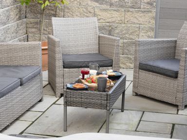 An outdoor seating area with rattan chairs and a table with food and mugs at Penpoll in Falmouth