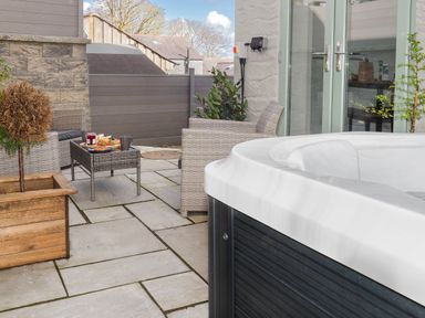 An outdoor patio area with a hot tub wicker chairs a table with food and a wooden planter at Penpoll in Falmouth