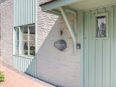 Front entrance of a building with a pale green door and window next to a textured white wall with a sign that says Porthallow at Porthallow in Mawnan Smith Near Falmouth