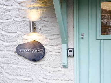 A stone wall with a light fixture and a sign that says Porthallow next to a light blue door at Porthallow in Mawnan Smith Near Falmouth
