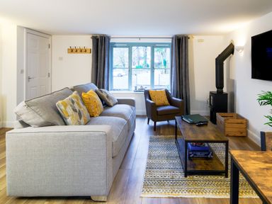 A living room with a grey sofa with pillows a brown armchair a wooden coffee table and a wall-mounted tv at Porthallow in Mawnan Smith Near Falmouth