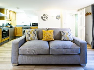 A kitchen and living area with a gray sofa and patterned cushions at Porthallow in Mawnan Smith Near Falmouth