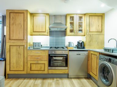 A kitchen with wooden cabinets a silver oven a dishwasher a washing machine and a kettle at Porthallow in Mawnan Smith Near Falmouth
