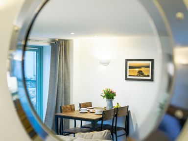 A dining room with a wooden table and chairs with flowers in a vase on the table at Porthallow in Mawnan Smith Near Falmouth