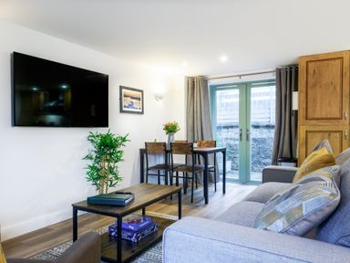 A living room with a sofa coffee table TV dining table and glass doors at Porthallow in Mawnan Smith Near Falmouth