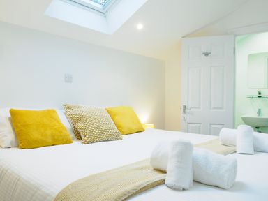 A bedroom with a bed with yellow pillows and rolled towels with a skylight window and an open door leading to a bathroom at Porthallow in Mawnan Smith Near Falmouth