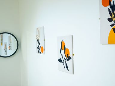 A white wall with two abstract botanical paintings and a round mirror reflecting the paintings at Porthallow in Mawnan Smith Near Falmouth