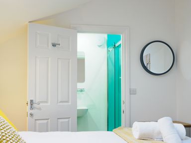 A bedroom with towels on a bed and an open door revealing a bathroom at Porthallow in Mawnan Smith Near Falmouth