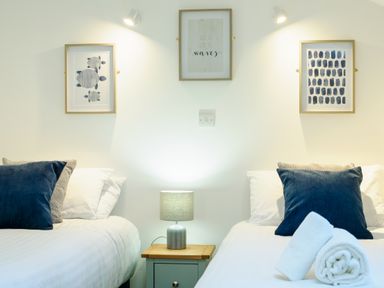 A bedroom with two single beds a nightstand lamp and framed pictures at Porthallow in Mawnan Smith Near Falmouth