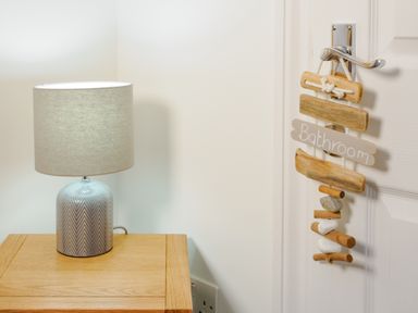 A lamp on a wooden table next to a door with a sign that says bathroom at Porthallow in Mawnan Smith Near Falmouth