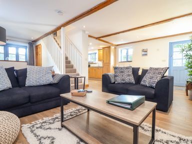 A living room with two black sofas pillows coffee table and visible kitchen area at St Keverne in Mawnan Smith Near Falmouth