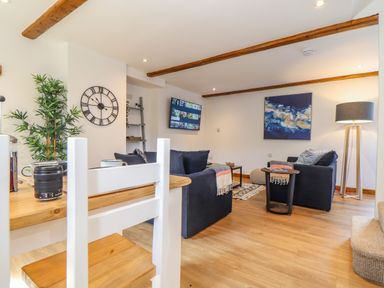 A living room with dark sofas a wall clock a floor lamp and a wall-mounted television at St Keverne in Mawnan Smith Near Falmouth