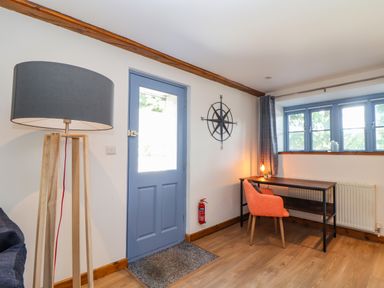 A room with a blue door wooden floor a floor lamp a desk with an orange chair and a compass wall decoration at St Keverne in Mawnan Smith Near Falmouth