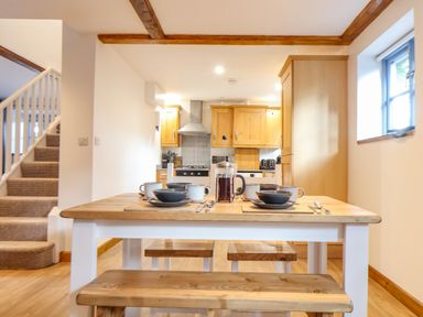 A kitchen with wooden cabinets and a dining table set with dishes and mugs at St Keverne in Mawnan Smith Near Falmouth