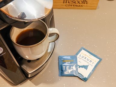 A coffee machine with a cup of coffee and sachets of tea and hot chocolate on a countertop at St Keverne in Mawnan Smith Near Falmouth