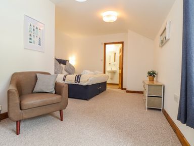 A bedroom with a brown armchair a bed and a small cabinet with a plant at St Keverne in Mawnan Smith Near Falmouth