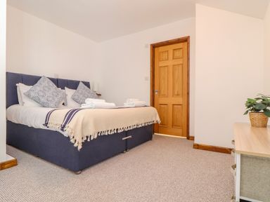 A bedroom with a double bed pillows folded towels wooden door and a plant on a dresser at St Keverne in Mawnan Smith Near Falmouth
