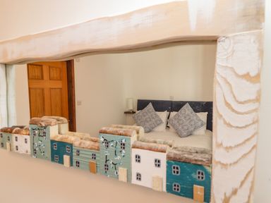 A bedroom with two patterned pillows on a bed reflected in a decorative mirror with small house designs at St Keverne in Mawnan Smith Near Falmouth