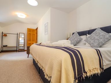 A bedroom with a bed covered in a blanket and rolled towels a mirror an open door and a clothes rack at St Keverne in Mawnan Smith Near Falmouth