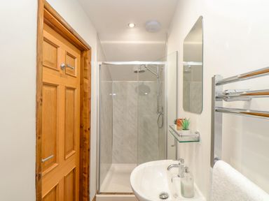 A bathroom with a wooden door glass shower enclosure showerhead sink with soap dispenser mirror and towel rack with a towel at St Keverne Mawnan Smith Near Falmouth