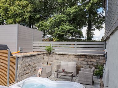An outdoor patio area with a hot tub table and chairs surrounded by stone and wooden fences at St Keverne in Mawnan Smith Near Falmouth