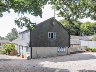 A two-story house with slate siding and blue-framed windows surrounded by trees and gravel driveway at St Keverne in Mawnan Smith Near Falmouth