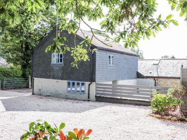 The exterior of a two story house with slate cladding and white lower walls surrounded by trees and gravel driveway at St Keverne in Mawnan Smith Near Falmouth