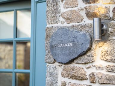 A stone plaque with the word Manacles mounted on a stone wall next to a blue window frame and a wall light at Manacles in Mawnan Smith Near Falmouth
