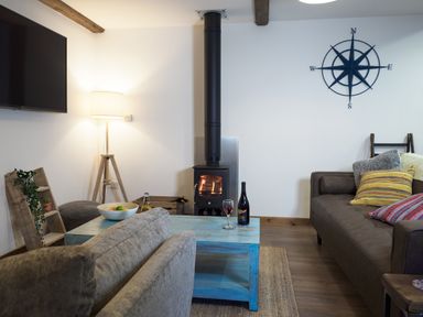 A living room with a wood stove wooden coffee table two sofas a floor lamp and a wall compass decoration at Manacles in Mawnan Smith Near Falmouth