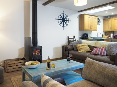 A living room with a wood-burning stove a blue coffee table and brown sofa at Manacles in Mawnan Smith Near Falmouth