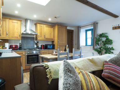 A kitchen with wooden cabinets a dining table and chairs and a brown sofa with cushions at Manacles in Mawnan Smith Near Falmouth