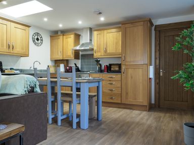 A kitchen with wooden cabinets a dining table with chairs a couch and a wooden door at Manacles in Mawnan Smith Near Falmouth
