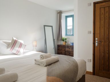A bedroom with a bed with towels a pillow a lamp a standing mirror a wooden chest of drawers and a window at Manacles in Mawnan Smith Near Falmouth