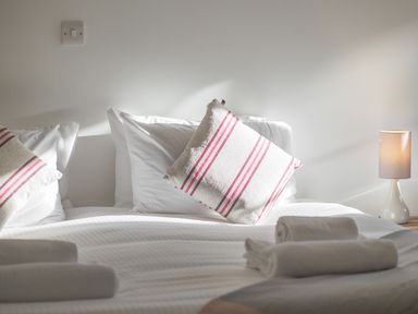 A bed with white linens pillows with red stripes and rolled towels next to a lamp at Manacles in Mawnan Smith Near Falmouth