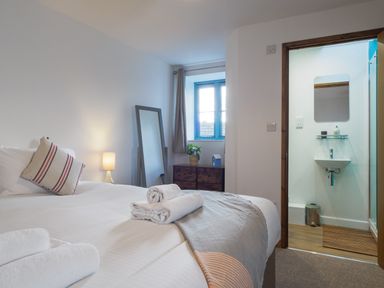 A bedroom with a bed towels a lamp a mirror window and an ensuite bathroom at Manacles in Mawnan Smith Near Falmouth