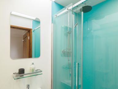 A bathroom with a glass shower enclosure and a rectangular mirror above a glass shelf at Manacles in Mawnan Smith Near Falmouth
