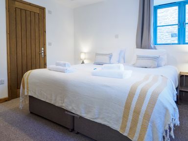 A bedroom with a double bed pillows rolled towels a wooden door and a blue window at Manacles in Mawnan Smith Near Falmouth
