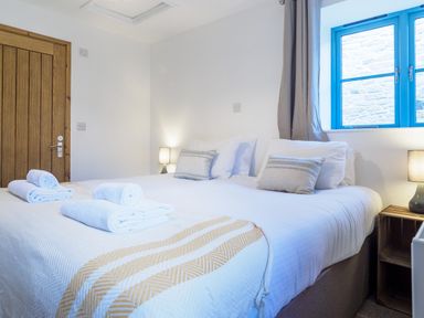 A bedroom with two single beds pushed together with pillows lamps and towels near a window with blue frame at Manacles in Mawnan Smith Near Falmouth
