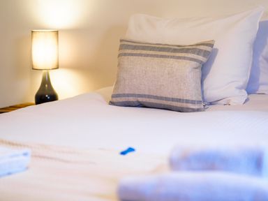 A bed with white pillows and a striped cushion next to a nightstand with a lamp at Manacles Mawnan Smith Near Falmouth