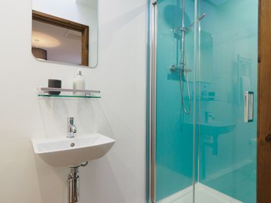 A bathroom with a wall-mounted sink a mirror and a glass-enclosed shower at Manacles in Mawnan Smith Near Falmouth