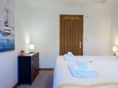 A bedroom with a wooden door a dresser with a lamp and towels on a bed at Manacles in Mawnan Smith Near Falmouth