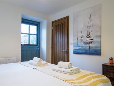 A bedroom with a bed with towels on a runner near a wooden door and a blue door with a window and a painting of sailboats on the wall at Manacles in Mawnan Smith Near Falmouth