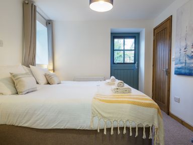 A bedroom with a double bed towels on the bed a wooden door and a window at Manacles in Mawnan Smith Near Falmouth