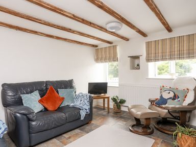 A living room with a leather sofa, armchair with footrest, small TV on a wooden table, and striped window blinds at Isfryn in Llanengan near Abersoch