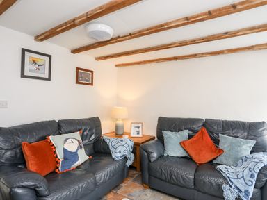 A sitting room with two black leather sofas cushions wooden beams on ceiling and a wooden side table with lamp at Isfryn in Llanengan near Abersoch