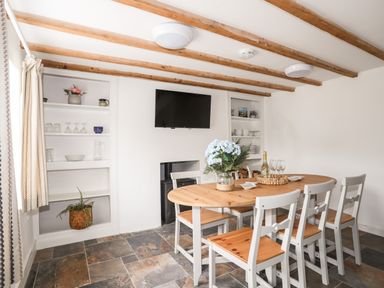 A dining room with a wooden table and chairs a television and shelves with dishes and plants at Isfryn in Llanengan near Abersoch