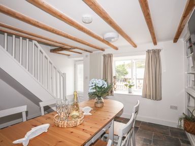 A dining area with a wooden table set with glasses and a bottle under wooden ceiling beams at Isfryn in Llanengan near Abersoch