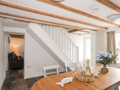 A dining area with a wooden table set with champagne and glasses under a staircase with wooden beams on the ceiling at Isfryn Llanengan near Abersoch