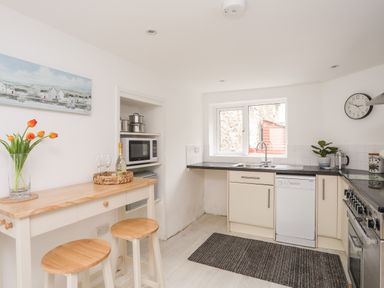 A kitchen with a wooden breakfast bar with stools a microwave oven a stove a dishwasher and a window at Isfryn Llanengan near Abersoch